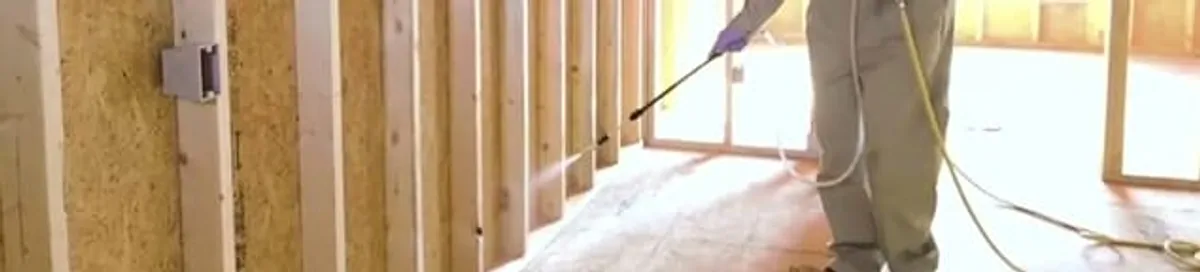 Termite treatment technician applying spray along framing and unfinished walls in Sterling Heights, MI